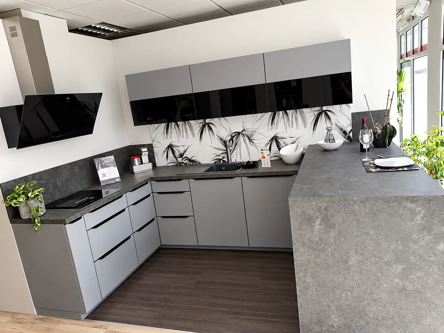 Musterküche U-Form in Grau mit Tresen in Betonoptik und Glasrückwand mit Bambus-Motiv – Gesamtansicht